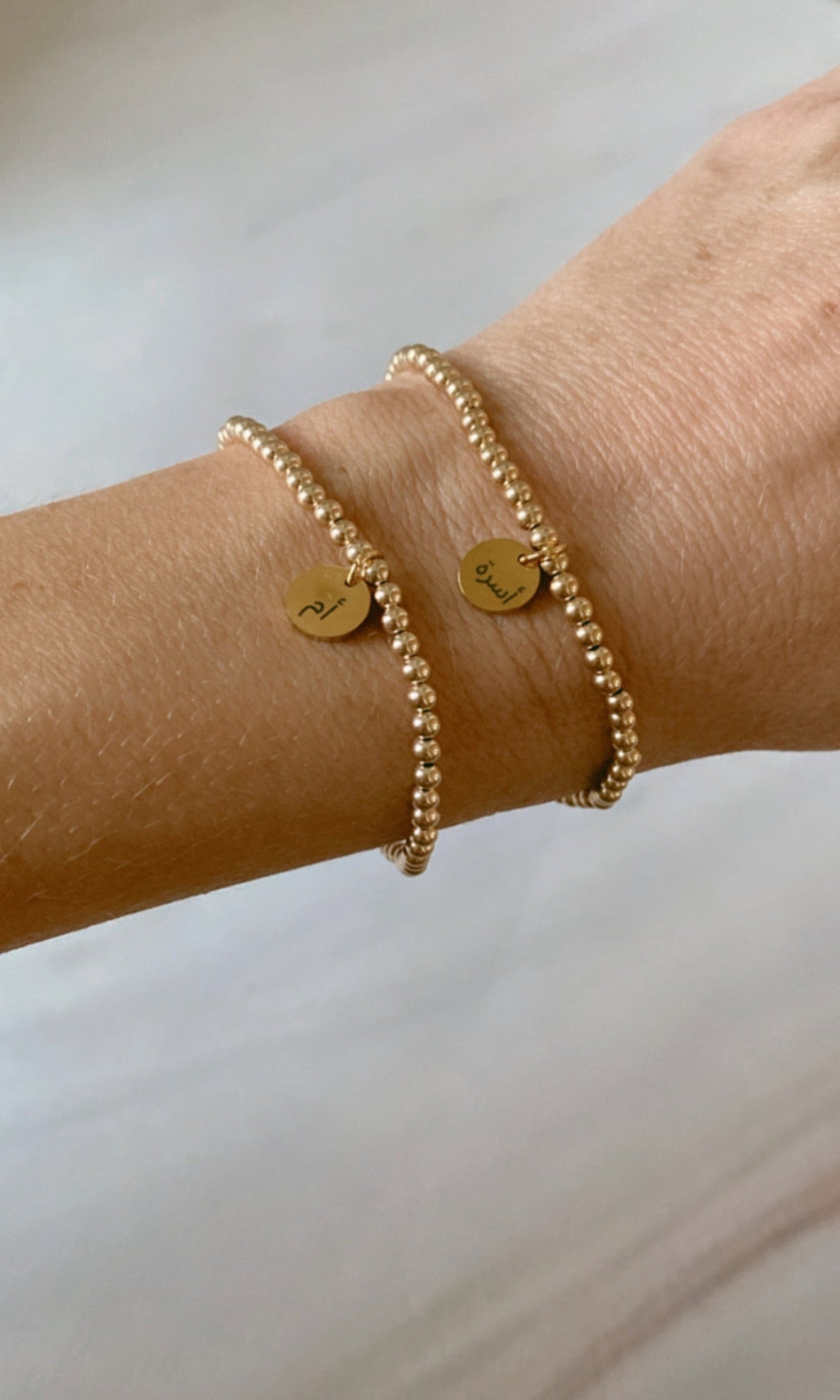 A gold-filled bracelet with two charms, one for each wrist, displayed on a person's forearm.